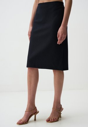 Gonna a matita nera al ginocchio con sottili righe verticali, vestibilità sartoriale e una texture di tessuto liscia. Abbinata a sandali con tacco nudo.