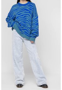 Blå stickad tröja med zebrastripesmönster, tillsammans med ljusblå vida jeans och svarta skor. Texturerad tyg, avslappnad passform.