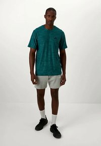 Tirkīza krāsas sporta krekliņš ar īsām piedurknēm un svītru rakstu, apvienots ar pelēkiem šortiem. Modelis valkā melnas kurpes un baltas zeķes.