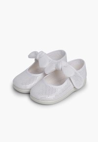 White perforated fabric shoes with a rounded toe, soft white strap and bow detail, and a flexible white rubber sole.