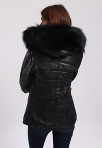 Svart läderjacka med avtagbar svart pälsmössa. Har quiltade paneler och en figursydd silhuett. Texturerad yta med slät finish.