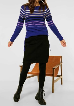 Blue and purple striped sweater with long sleeves, paired with a black skirt and black leggings. Black lace-up combat boots, wooden chair in background.