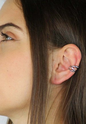 Silver ear cuff with a twisted design, positioned on the upper part of an ear, accompanied by long, straight brown hair.