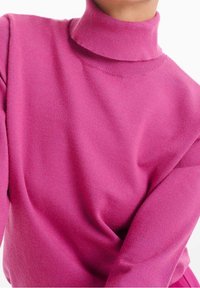 Polotröja i livfull rosa, med en mjuk textur, avslappnad passform och ribbade detaljer på kragen och manschetterna.