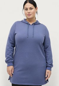 Vestido sudadera azul con mangas largas, cordón ajustable y aberturas laterales. Tela suave, corte relajado y diseño a la altura de la cadera.