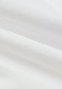 Gros plan d'un tissu blanc plié montrant une texture fine tissée et de légers plis.