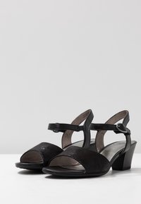 Svarta öppetåda sandaler med en texturerad mockafront, blanka läderremmar och en blygsam klack. Utrustad med en justerbar ankelrem och en vadderad innersula.