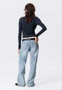 Marineblaues Langarmshirt kombiniert mit hellblauen, locker sitzenden Jeans. Das Shirt ist tailliert geschnitten; die Jeans haben ein klassisches Fünf-Taschen-Design und einen schwarzen Gürtel.