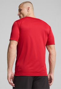 Camiseta atlética roja de manga corta con tela suave, diseño ajustado y cuello redondo. La vista trasera muestra costuras planas y detalles en los hombros.