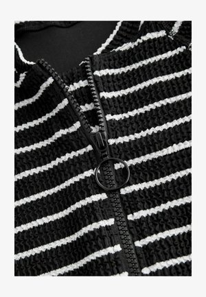 Fekete-fehér csíkos anyag, texturált, ráncolt kialakítással. Középen fekete cipzárral, kerek húzóval.