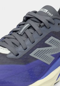 Αθλητικό παπούτσι με γκρι πλέγμα στο πάνω μέρος, μωβ λεπτομέρειες και υφασμένη σόλα. Διαθέτει έντονο γκρι λογότυπο και επίπεδα κορδόνια.