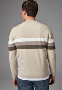 Suéter de punto beige con rayas horizontales en blanco, marrón claro y marrón oscuro. Mangas largas y cuello redondo. Jeans de mezclilla visibles.