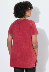 Rode t-shirt met korte mouwen in een gewassen textuur, met zijsplitten en een afgeronde zoom. De stof lijkt zacht en casual.