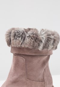 Natural suede brown boot with a soft, faux fur cuff. The boot has a rounded shape and stitched detailing along the edges and ankle.