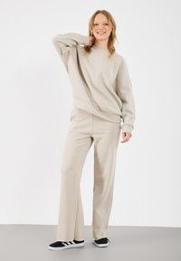 Beige sweatshirt en bijpassende broek, gemaakt van zachte stof, met een relaxte pasvorm. Voorzien van lange mouwen, geribbelde manchetten en uitlopende broekspijpen.