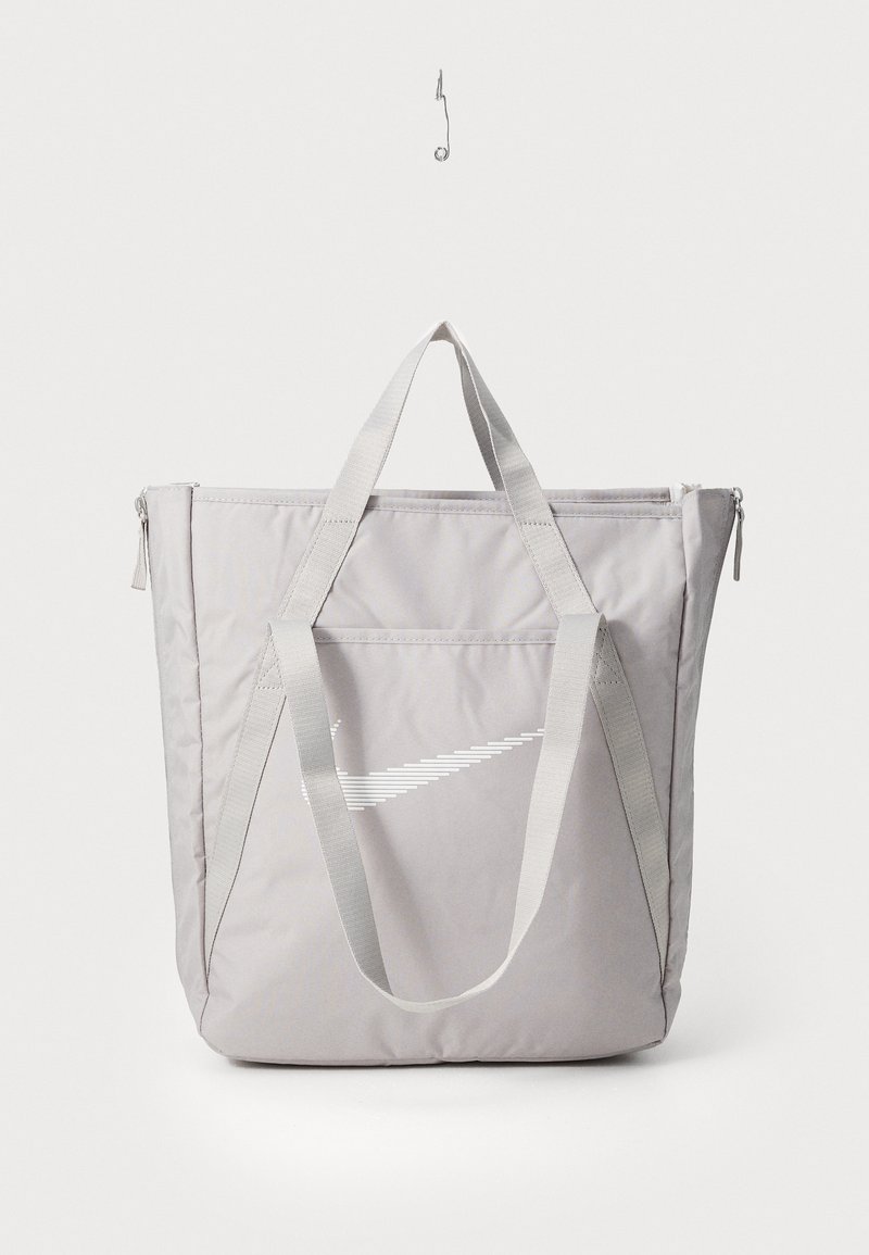Sac fourre-tout gris avec des poignées renforcées, poche zippée à l'avant et logo Swoosh Nike blanc. Fabriqué en tissu durable avec une texture lisse.