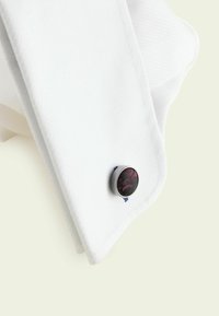 Weißer, strukturiert texturierter Hemdärmel mit einer runden, dunklen Stoffmanschettenknopf, der ein dezentes rotes Blumenmuster aufweist.