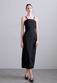 Black sleeveless dress with a fitted bodice, straight skirt, and subtle pleats. Smooth fabric texture with minimal design details.