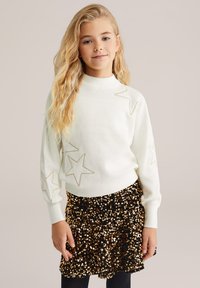 Pulover alb, cu o textură striată, brodat cu stele aurii și cu mâneci lungi, asociat cu o fustă neagră acoperită cu paiete aurii.