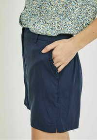 Shorts bleu marine avec poches latérales, présentant une texture lisse et une coupe décontractée. Détail subtil de plis aux bords des poches.