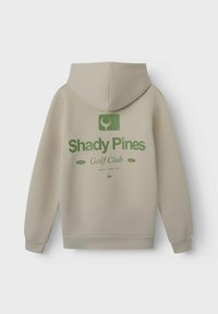 Bež hoodie s kapuljačom s zelenim grafičkim logotipom koji na leđima glasi "Shady Pines Golf Club". Mekani materijal s rebrastim manžetama.
