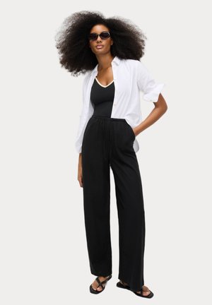 Black wide-leg pants with a drawstring waist, paired with a black tank top and an open white button-up shirt. Accessories include black sunglasses.