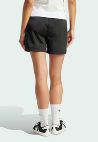 Černé atletické šortky s hladkou texturou, středním pasem a bočními švy. Nošeny s bílými ponožkami a černými teniskami.