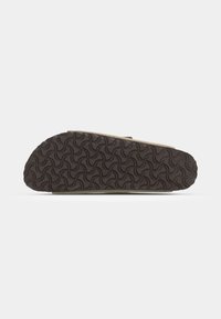 Semelle en caoutchouc marron avec un motif de traction ondulé ; section supérieure beige visible, avec une texture lisse et des détails de design minimes.