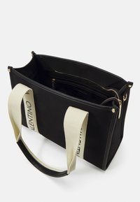 Schwarze Leinenshoppingtasche mit goldenen Beschlägen, dualen cremefarbenen Griffen mit Logodetails und einem offenen Innenraum, der eine Reißverschlusstasche zeigt.