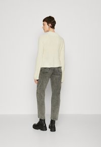 Maglione lavorato a maglia di colore panna con una texture a coste, abbinato a jeans grigi attillati e stivaletti neri con suola spessa.