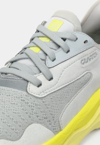 Grå sneakers med texturerad mocka och meshöverdrag, accentuerad av en klar gul sula och logotyp. Har grå snören och syntetiska overlay.