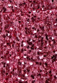 Vaaleanpunainen kangas, joka on peitetty pienillä pyöreillä paljeteilla, jotka heijastavat valoa; se esittää tekstuurista, kiiltävää ilmettä vaihtelevine vaaleanpunaisen sävyineen.