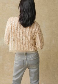 Top transparent nude avec des motifs de feuilles brodés ; associé à un jean en denim bleu clair, présentant une coupe droite et des poches standards.