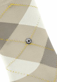 Beige og grå mønstret sok med diamantdesign, struktureret overflade og gule stropper, med en rund logoアクセ.