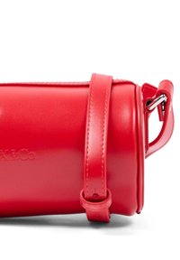 Borsa cilindrica rossa in pelle con tracolla regolabile e fibbia in metallo argentato, logo in rilievo parzialmente visibile sulla superficie liscia.