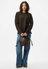 Brązowy sweter dzianinowy o luźnym kroju i bocznych rozcięciach. Jasnoniebieskie spodnie o szerokich nogawkach. Ciemnobrązowa skórzana torba typu bucket z otworem w kształcie V.