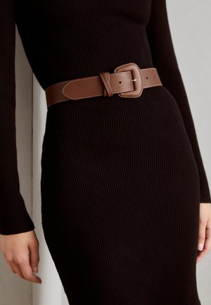 Close-up van een persoon die een zwarte geribbelde jurk draagt met een brede bruine leren riem die om de taille is vastgemaakt.