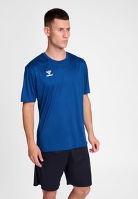 Kék sportpóló, nedvességelvezető anyagból, rövid ujjal és kerek nyakkivágással. A márkázott logó a bal mellrészen látható.