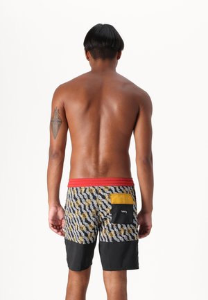 Bañador colorido con un cuerpo principal estampado en negro, blanco y amarillo, con una cinturilla roja y un detalle de bolsillo amarillo.