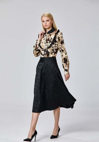 Blouse florale avec un col volanté, tons beige et marron, associée à une jupe évasée noire avec un motif texturé et des talons hauts.