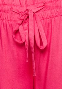 Tecido leve e rosa com uma textura suave. Apresenta um cós elástico e um cordão amarrado, criando um ajuste descontraído.