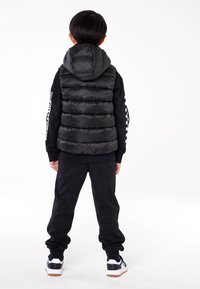 Czarna pikowana kamizelka z kapturem, z poziomym przeszyciem. Noszona na czarnym swetrze i spodniach, uzupełniona białymi trampkami.