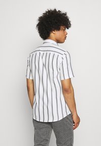 Short-sleeve, white shirt with gray vertical stripes, fold-down collar, and back yoke detail, paired with gray plaid trousers.