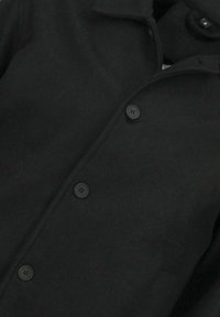 Zwarte wollen jas met een klassieke kraag, knoopsluiting aan de voorkant en vier bijpassende knopen. Gladde textuur met een getailleerde pasvorm.