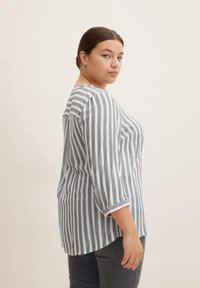 Camisa de rayas gris y blanca con mangas 3/4, escote redondo y puños enrollados. Tejido suave con un corte holgado, bajo curvado en la parte posterior.
