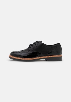 Zwarte leren oxford schoen met lakglans en brogue-details, voorzien van ronde veters en een textuurzijpaneel, geplaatst op een bruine zool.