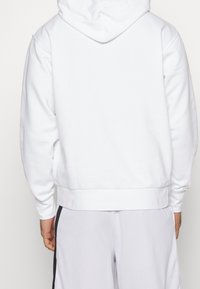 Felpa con cappuccio bianca in cotone, dal taglio comodo, con polsini e orlo ribattuti e una consistenza liscia. La vista posteriore non presenta grafiche.