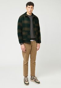 Grøn og brun rutig jakke med to forlommer, grå sweatshirt, beige bukser og multicolore sneakers med en tekstureret sål.