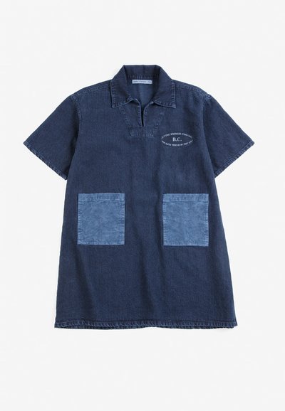 Robe en jean bleu foncé à manches courtes avec col, deux poches avant bleu clair et petit texte blanc sur la partie supérieure gauche de la poitrine.