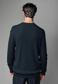 Texturiertes schwarzes Sweatshirt mit einem einzigartigen Waffle-Muster, mit rundem Halsausschnitt sowie geripptem Saum und Bündchen, von hinten gezeigt.